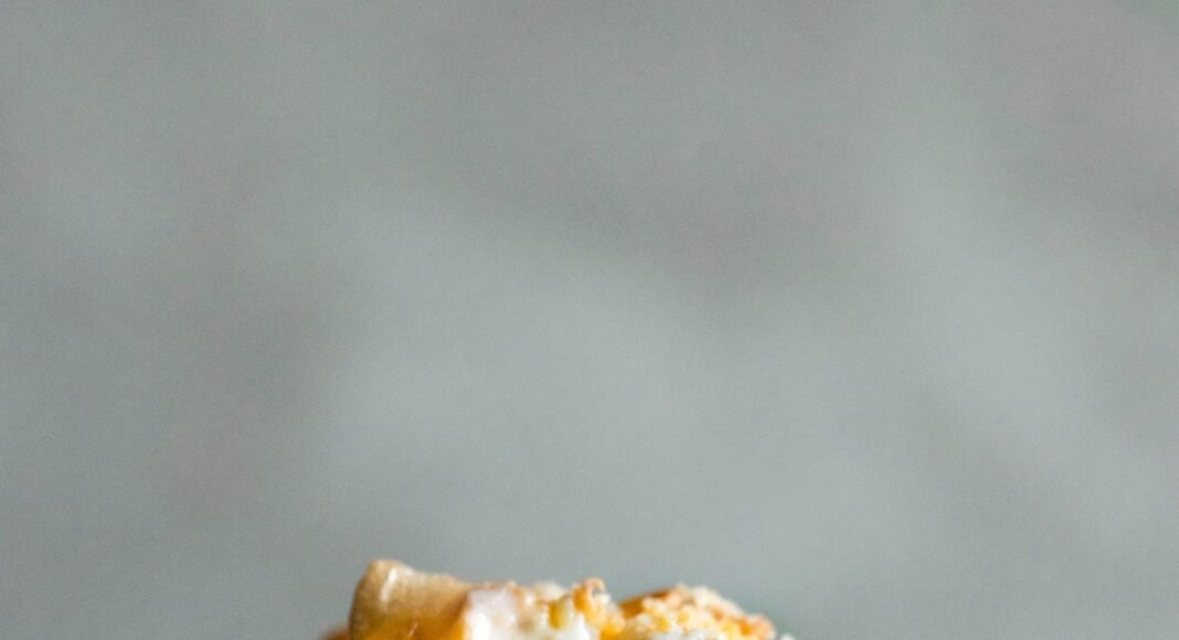 A spoon lifting a serving of cheesy chicken hashbrown casserole from a baking dish.