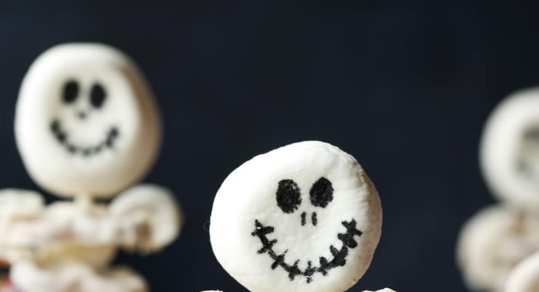 A halloween cupcake topped with a skeleton made from marshmallows and white chocolate covered pretzels