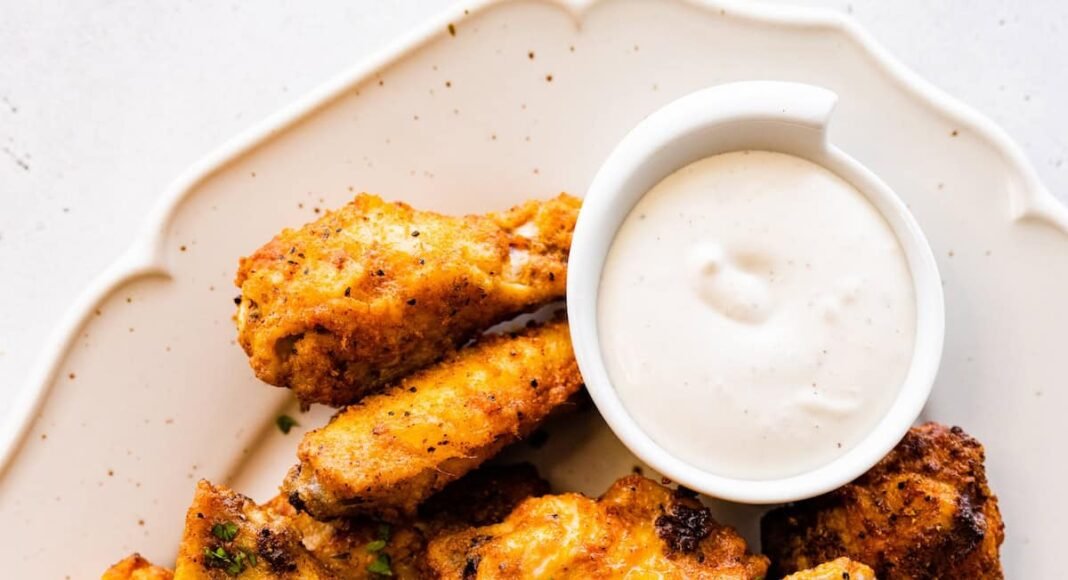A large plate of air fried chicken wings topped with fresh herbs with a side of ranch.
