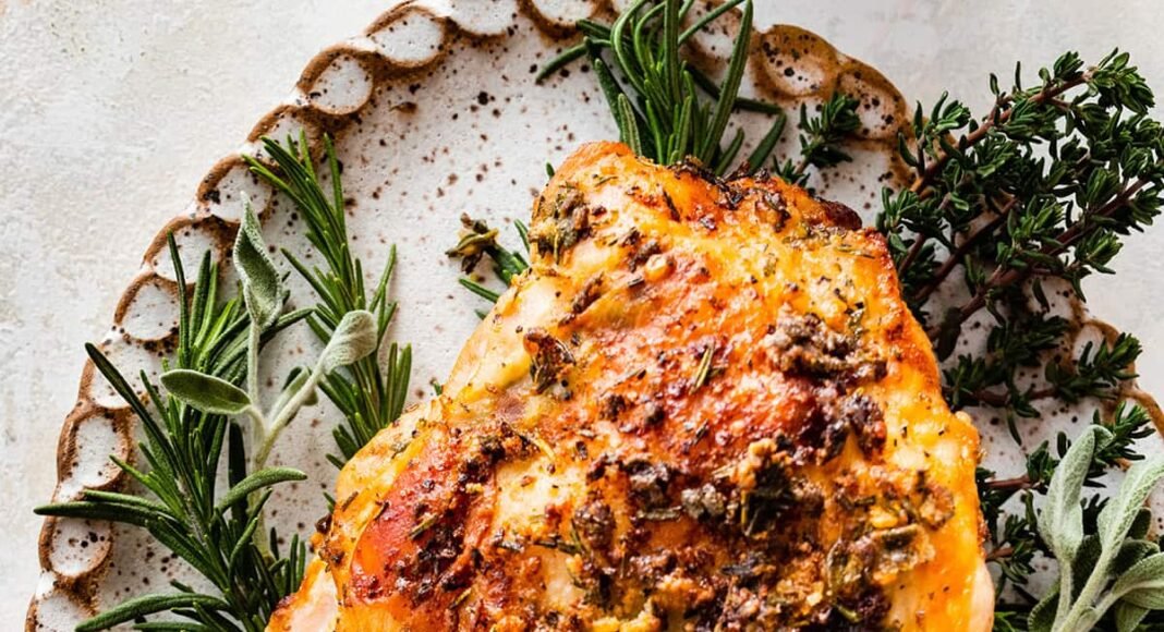 An air fryer turkey breast sliced sitting on a bed of fresh herbs and cranberries on a white platter.