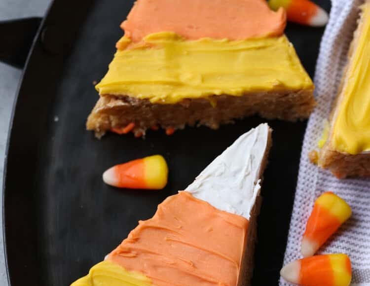 Scotcheroos shaped and decorated like candy corn on a plate next to candy corn pieces.