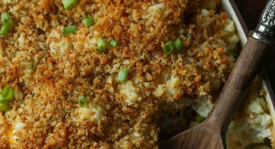 A cheesy cauliflower casserole with portions scooped out, and a wooden spoon resting in the dish.