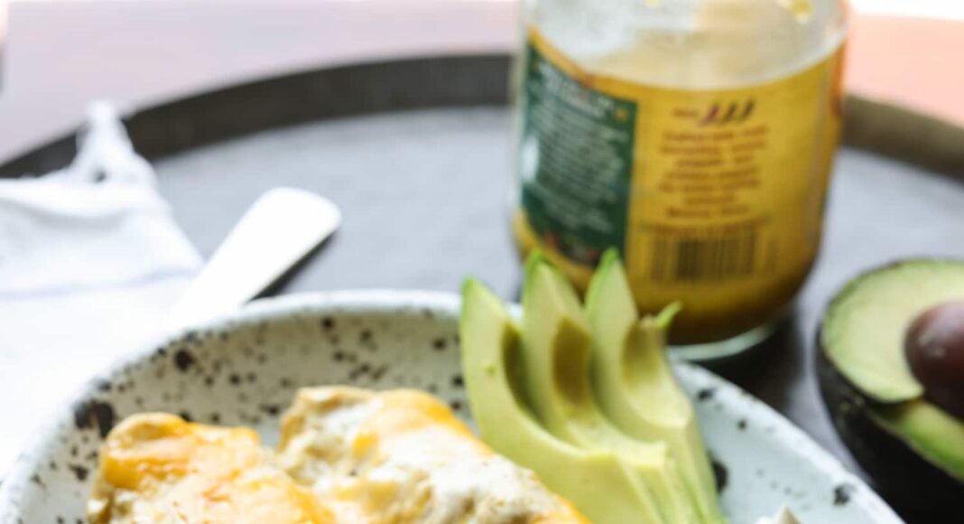 Chicken Enchiladas on a serving plate covered in melted cheese with avocado slices