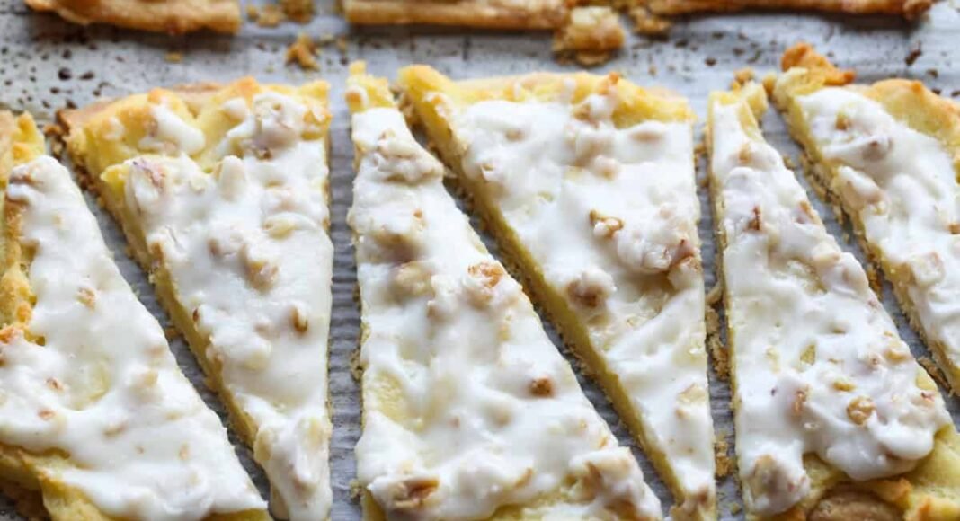 Danish Krisgle cut into slices topped with walnuts and icing on a parchment lined baking sheet
