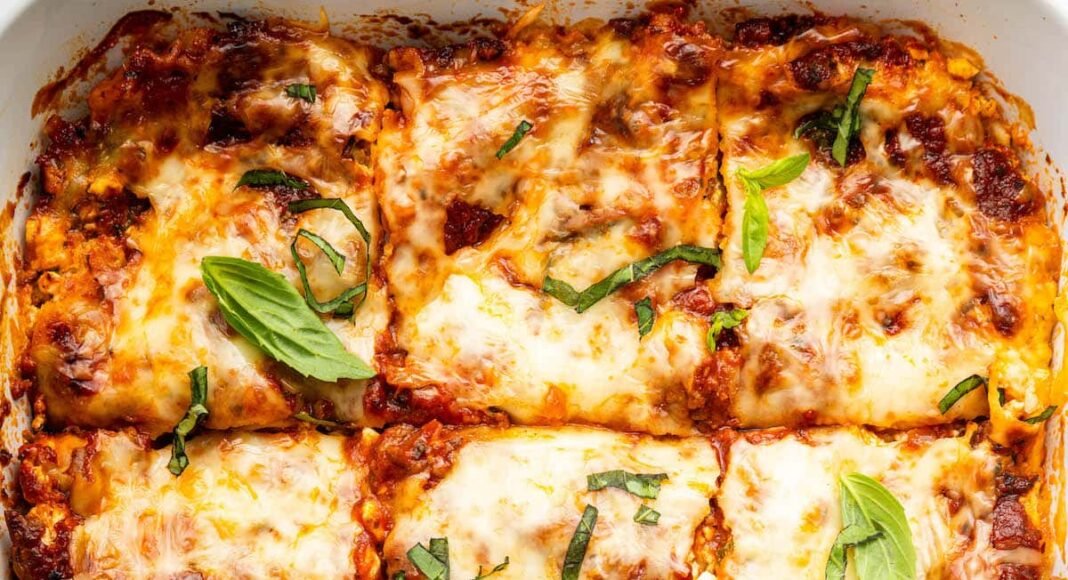 Healthy lasagna in a baking dish, cut into squares, and garnished with fresh basil and parsley.