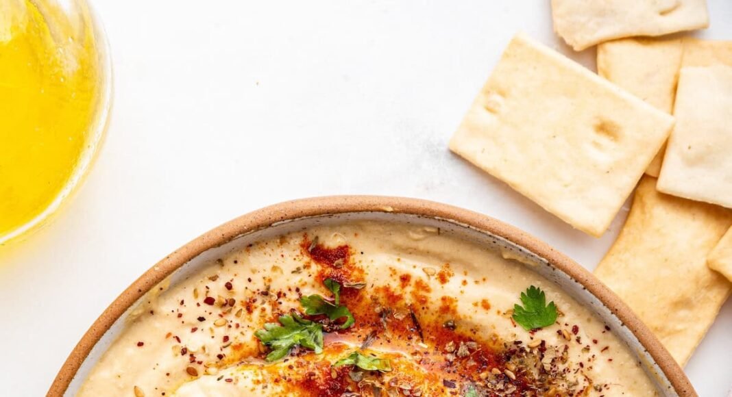 A bowl of creamy hummus topped with olive oil, herbs, and spices.