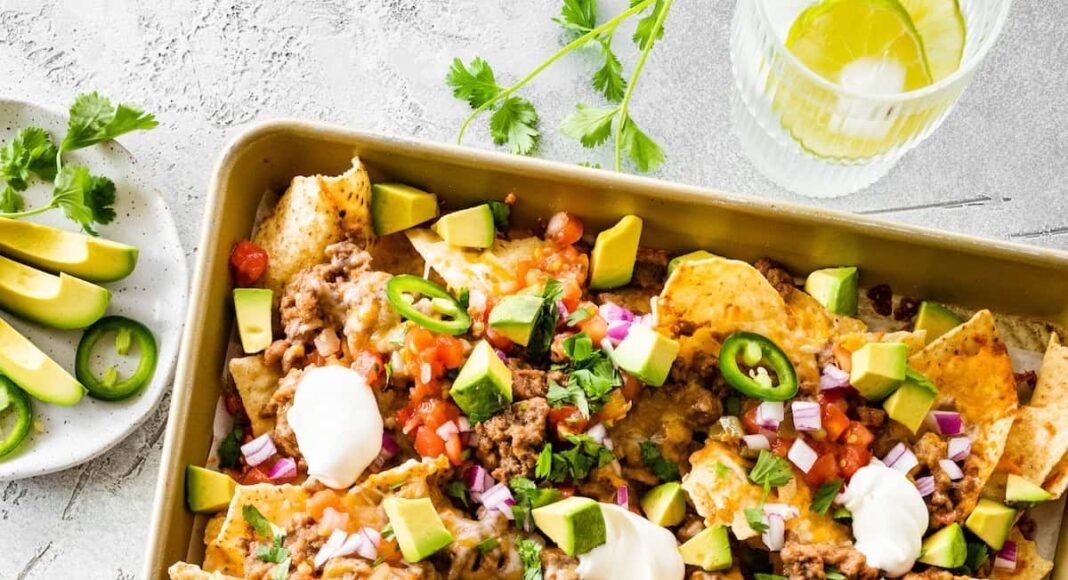Loaded nachos on a baking tray with meat, jalapeños, sour cream, avocado, cheese, and more.