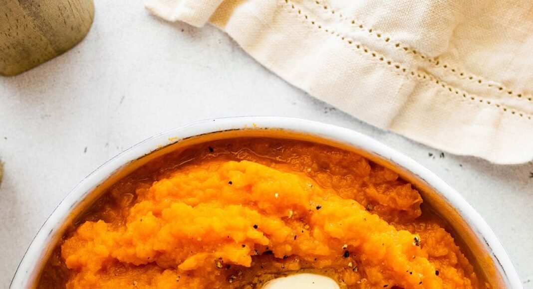 Mashed sweet potato in a bowl topped with two slices of butter and seasonings.