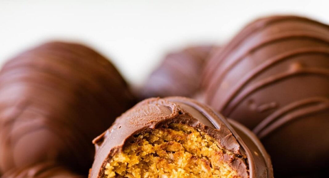 Chocolate covered peanut butter balls in a bowl with one ball having a bite taken from it.