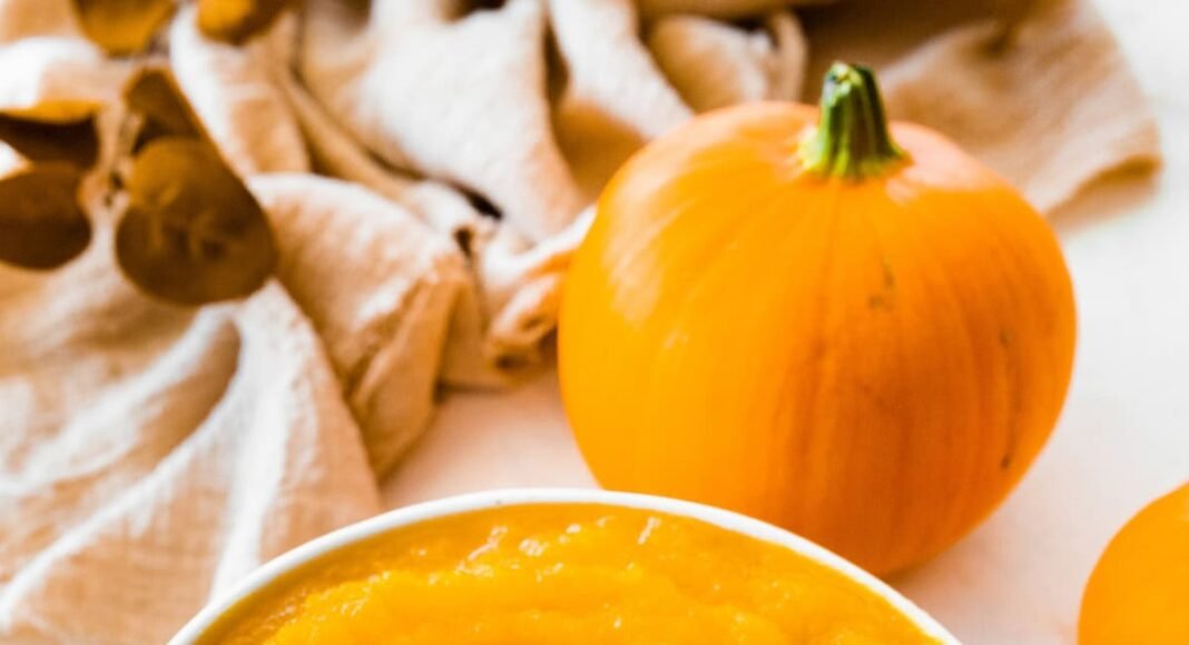 A homemade pumpkin puree in a bowl on a circular wooden board.