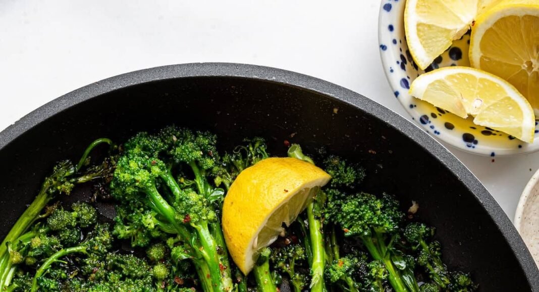 A pan of saut&eacute;ed broccolini with lemon wedges and red pepper flakes.