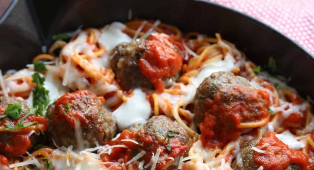 Spaghetti and Meatballs baked in a skillet topped with cheese and fresh parsley