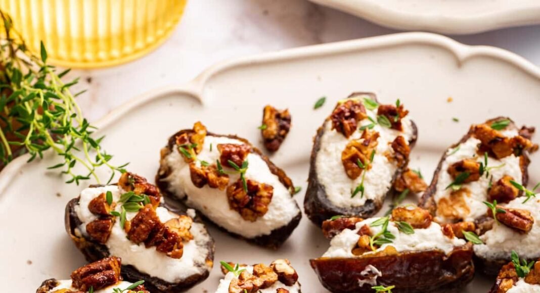 A large plate of multiple dates that are stuffed with goat cheese and topped with chopped pecans and fresh thyme.