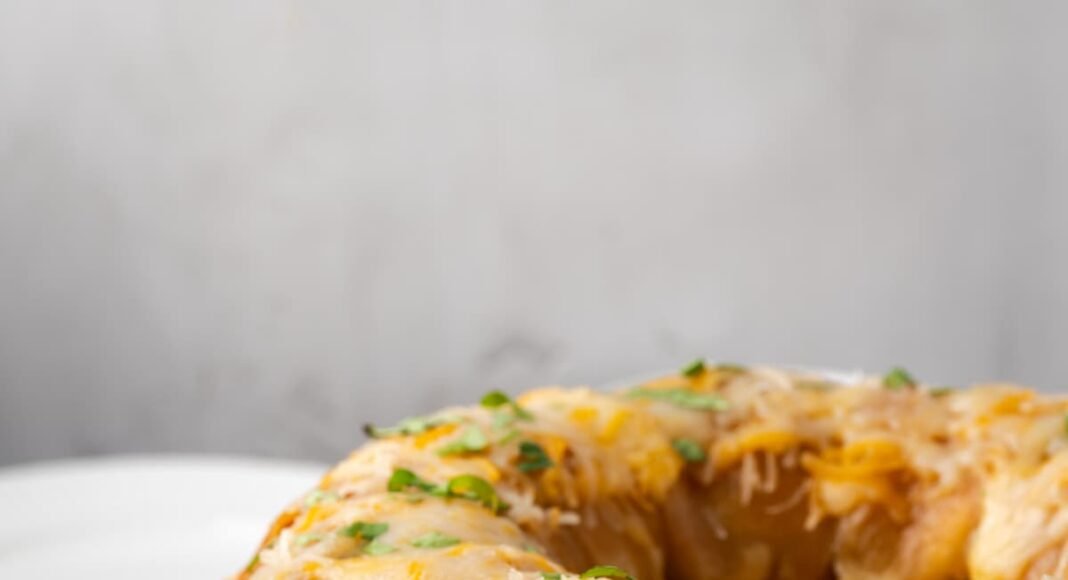 Taco monkey bread topped with melted cheese on a white plate, next to a bowl of shredded lettuce.