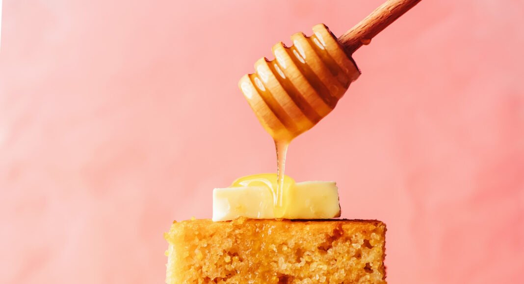 Drizzling honey onto a stack of gluten-free cornbread slices topped with butter