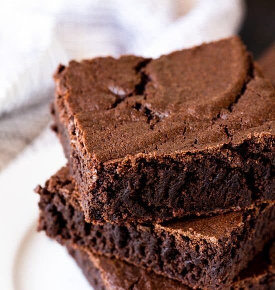 Three squares of the most amazing brownies stacked on top of each other on a white plate