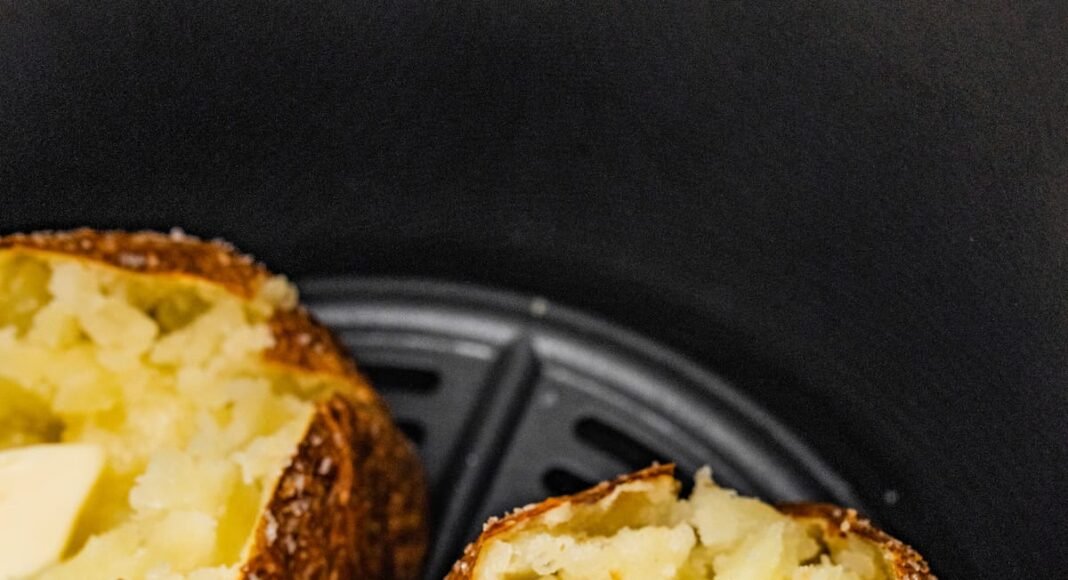 Three air fryer baked potatoes sliced open with butter in an air fryer.