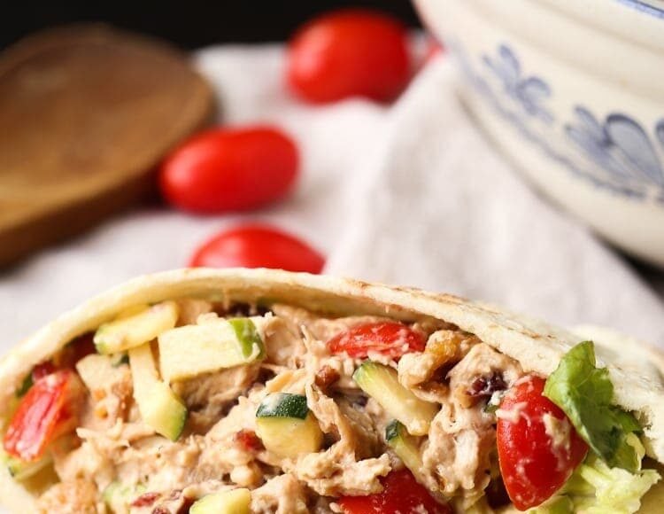 A crunchy chicken salad inside of a piece of pita bread on a table with cherry tomatoes