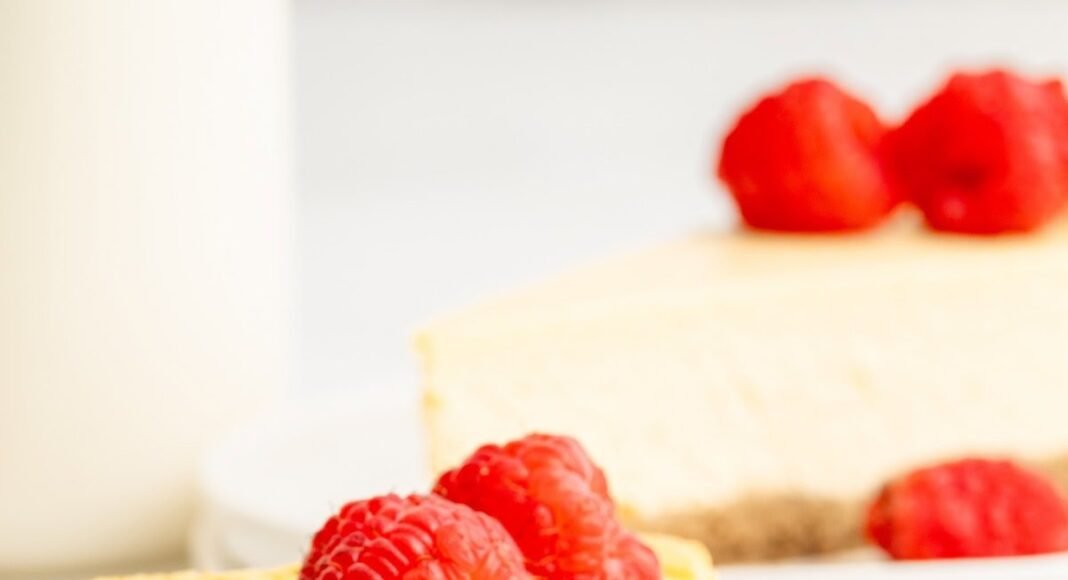 A slice of healthy cheesecake served on a white plate topped with fresh raspberries. A bite has been taken out of the slice.