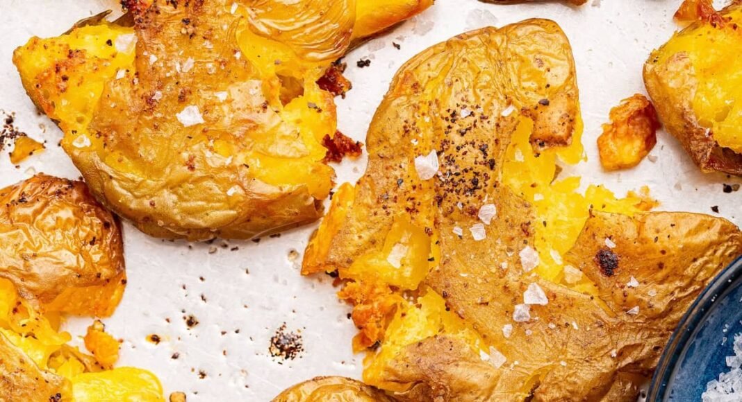 Seasoned and salted smashed potatoes on a baking tray.