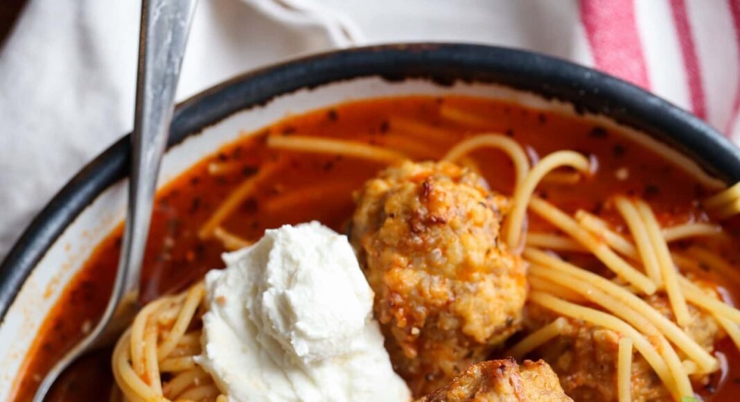 Bowl of spaghetti and meatball soup topped with parmesan cheese and ricotta