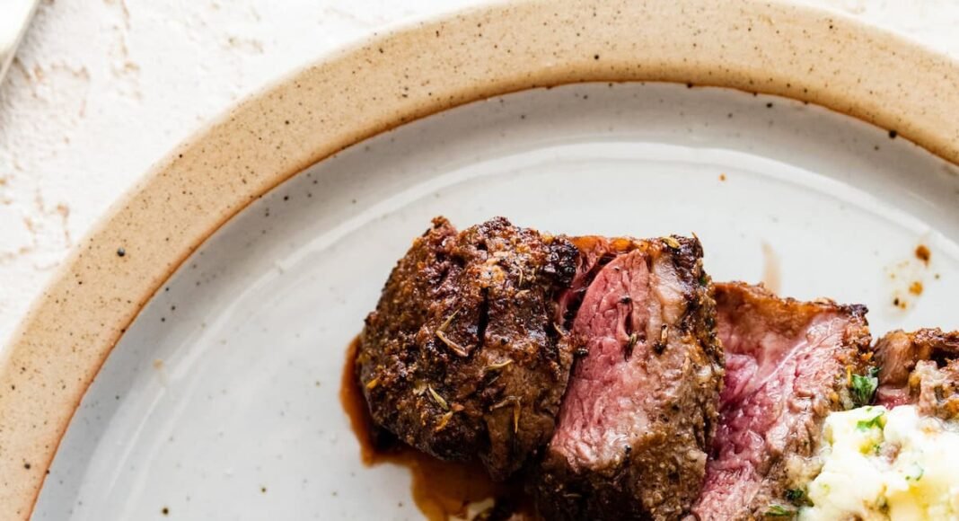 Two filet mignon pieces sliced on a white plate topped with garlic butter.