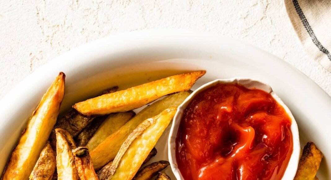 A plate of air fryer french fries with a small container of ketchup on the side.