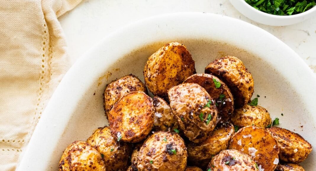 Crispy air fryer potatoes on a white plate garnished with fresh herbs and flaky sea salt.