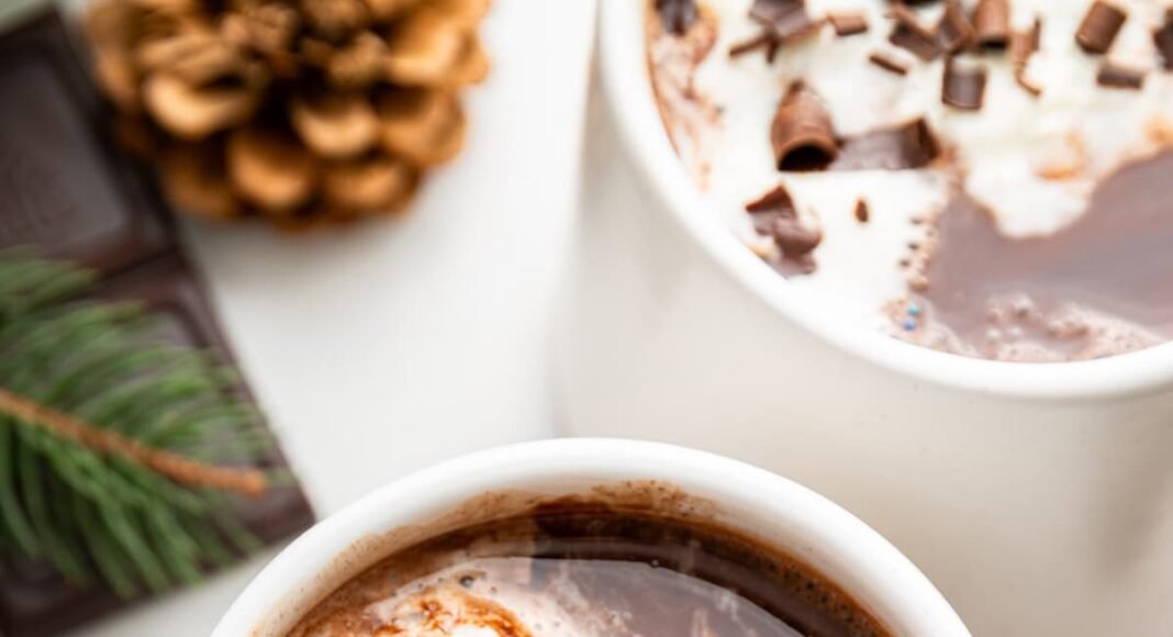 Two white mugs of hot chocolate topped with a little whip cream and chocolate shavings.