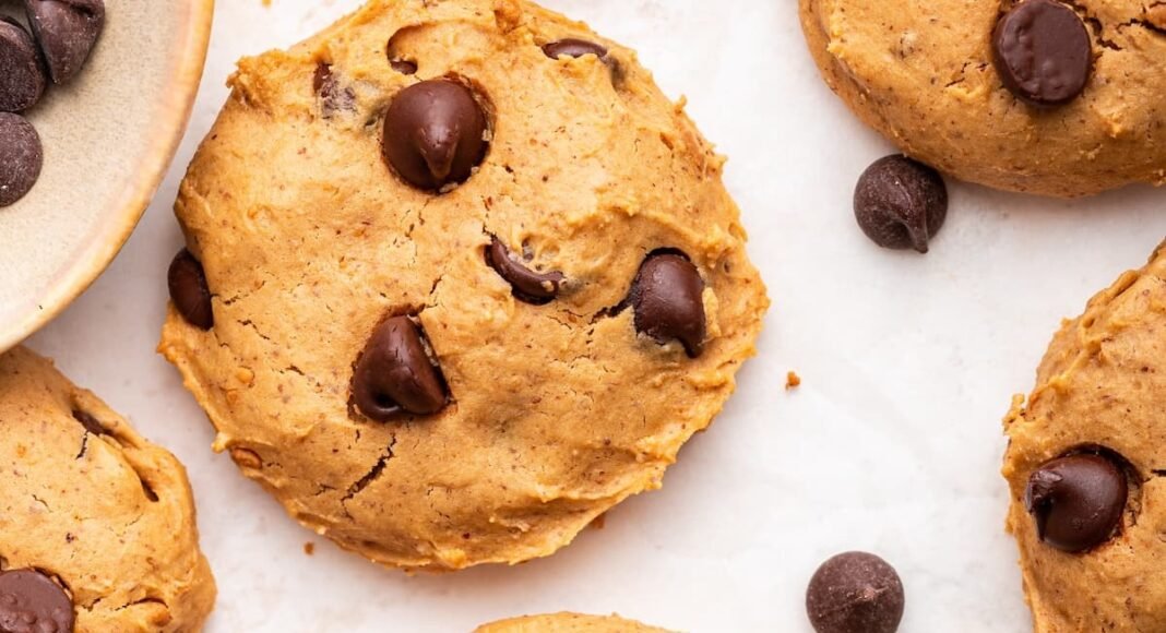 Multiple chocolate chip protein cookies are spread out on a countertop.