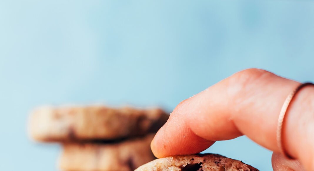 Holding up a vegan gluten-free chocolate chip pecan shortbread cookie with a stack of cookies behind it