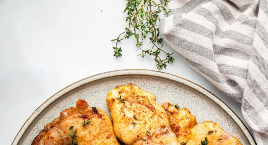 Baked boneless chicken thighs on a plate, garnished with fresh herbs.