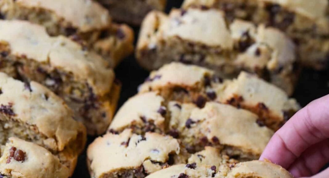 A hand taking a piece of biscotti from a serving tray
