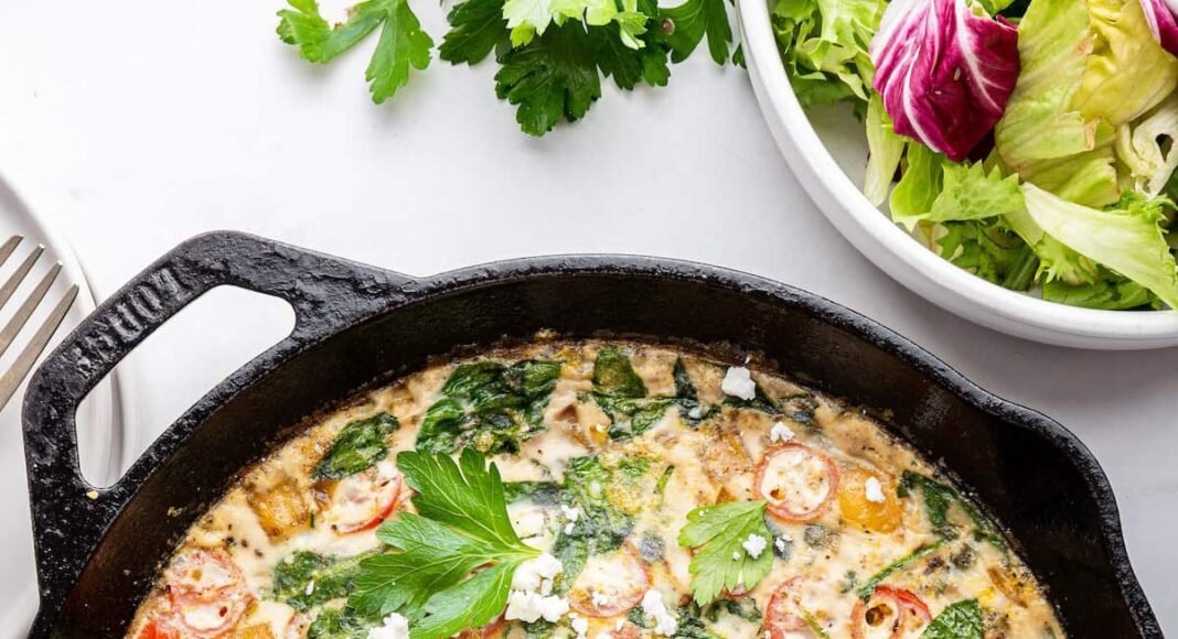 An egg white frittata in a cast iron skillet. The frittata is garnished with fresh herbs and feta cheese.