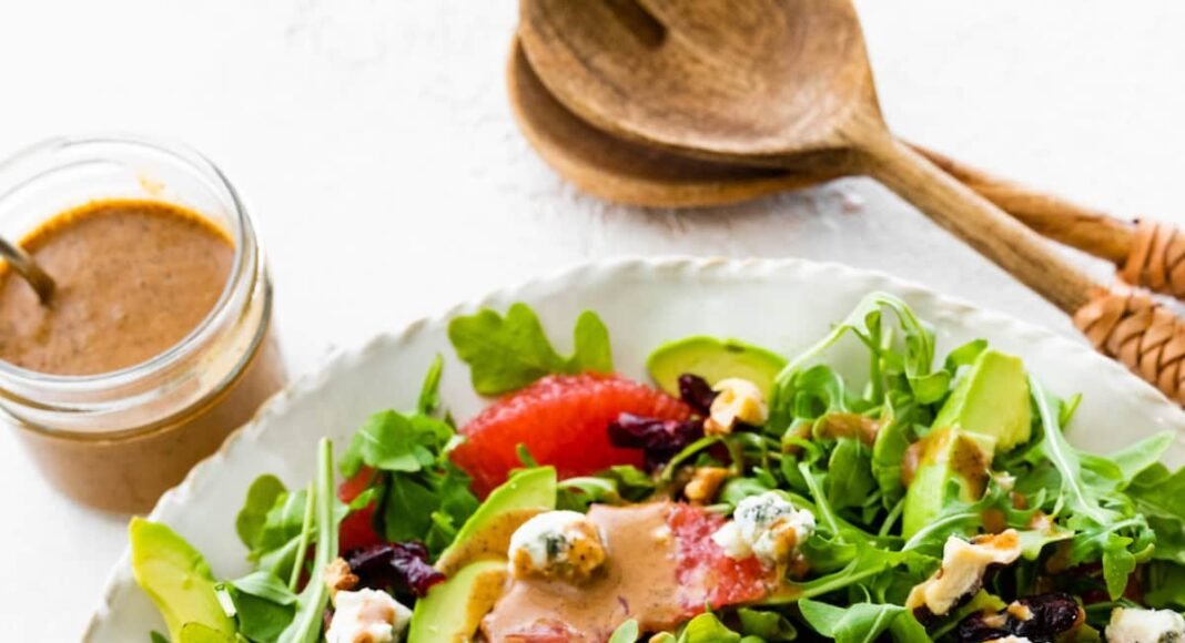 A salad with arugula, avocado, blue cheese, grapefruit, nuts, and cranberries on a white plate.