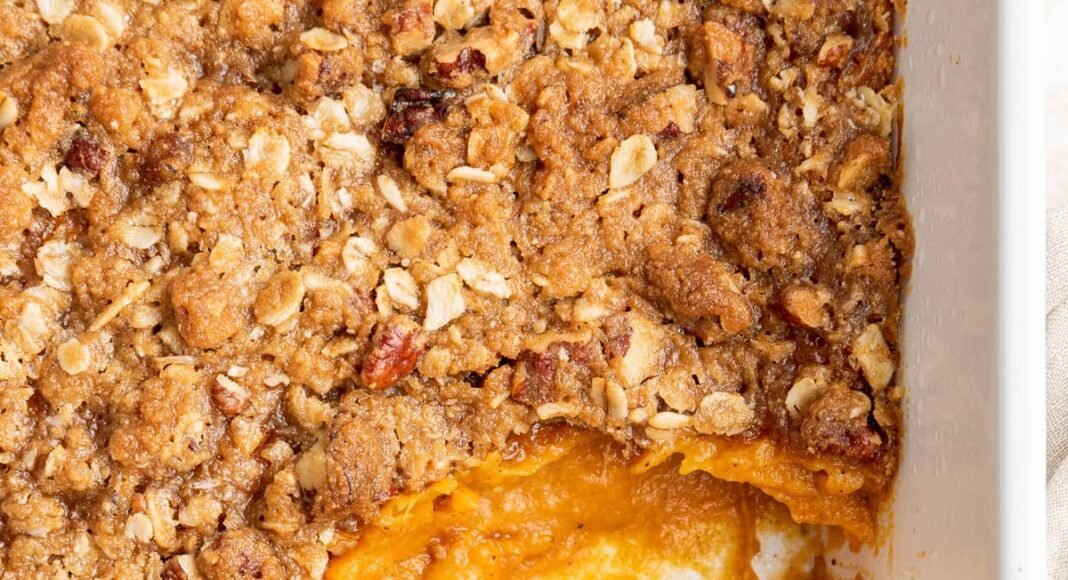 A serving spoon resting in a white baking dish containing sweet potato casserole.