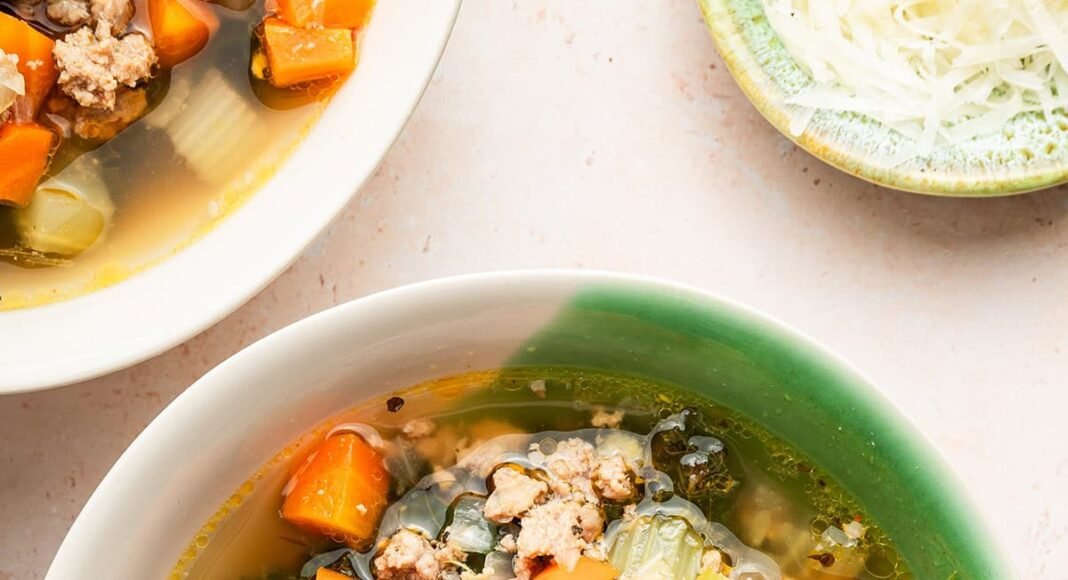 Sausage and kale soup served up in a green and white soup bowl.