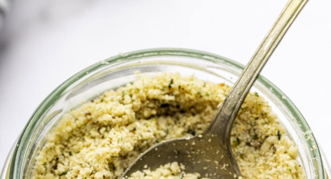 A vegan parmesan cheese made with hemp seeds in a glass mason jar with a metal spoon.