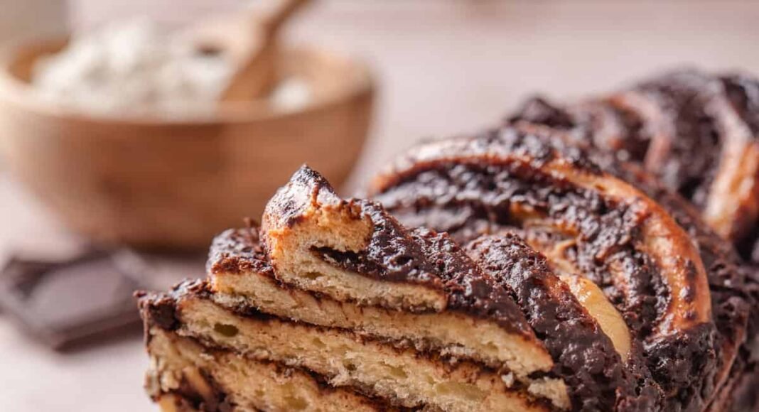 A chocolate babka on a long plate with a slice cut from the end.
