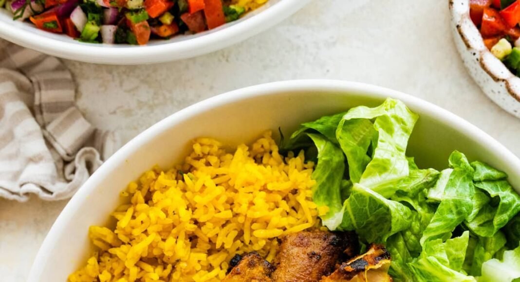 A chicken shawarma bowl with turmeric rice, sliced chicken shawarma, romaine lettuce, Shirazi salad, hummus and Toum.
