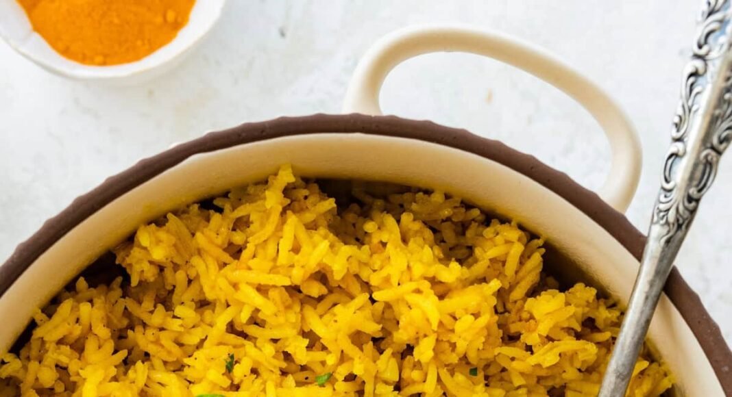 A pot of cooked turmeric rice topped with fresh parsley. There is a silver spoon in the rice.