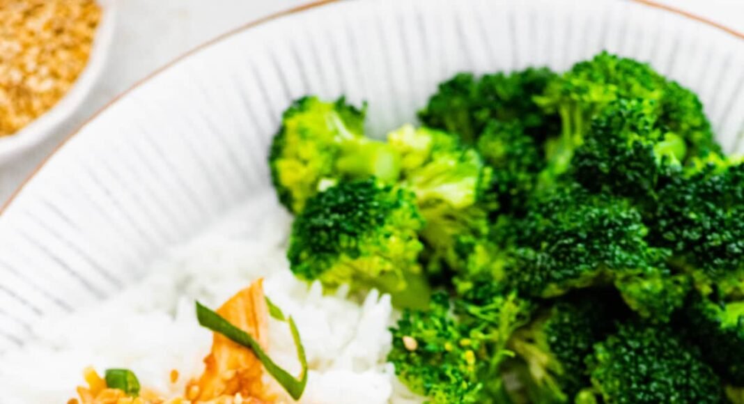 Slow cooker teriyaki chicken served on a plate with white rice and broccoli. The chicken is topped with sesame seeds and green onions.