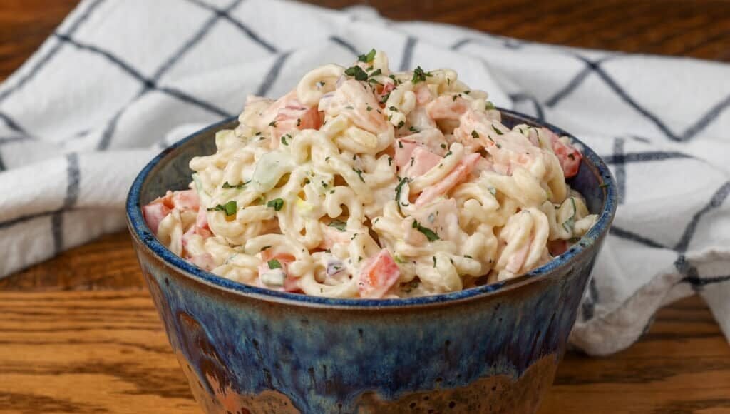 shrimp pasta salad in a pottery bowl with a white and blue patterned linen