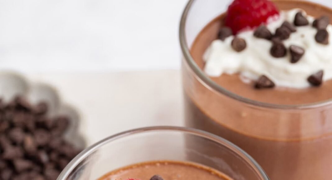 Cottage cheese chocolate mousse in two glasses topped with whip cream, chocolate chips and fresh raspberries.