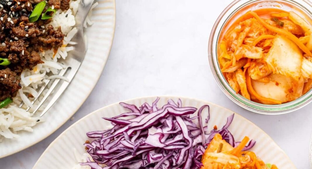 Korean beef served over white rice with fresh carrots, purple cabbage, cucumber and kimchi. The beef is topped with sesame seeds and green onions.