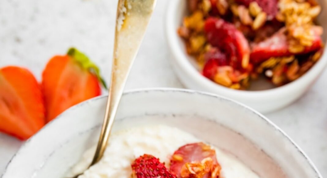 Cottage cheese in a bowl topped with roasted strawberries, rolled oats and coconut. There is a silver spoon in the bowl.