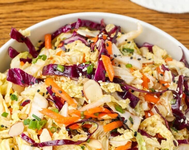 multi color Asian cabbage salad in a white bowl on a wooden surface with a blue and white linen
