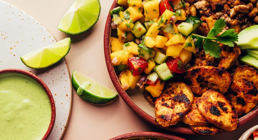 Drizzling green tahini sauce onto a Jerk Tofu & Roasted Plantain Bowl