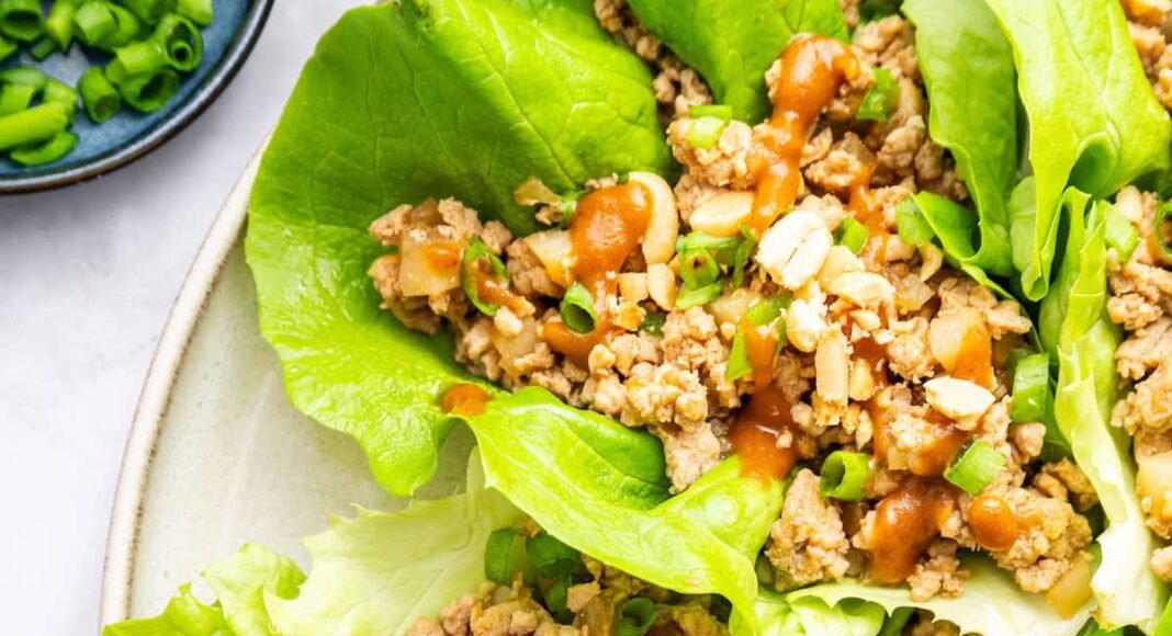 Ground chicken lettuce wraps served on a plate with a peanut sauce drizzle and fresh green onions.