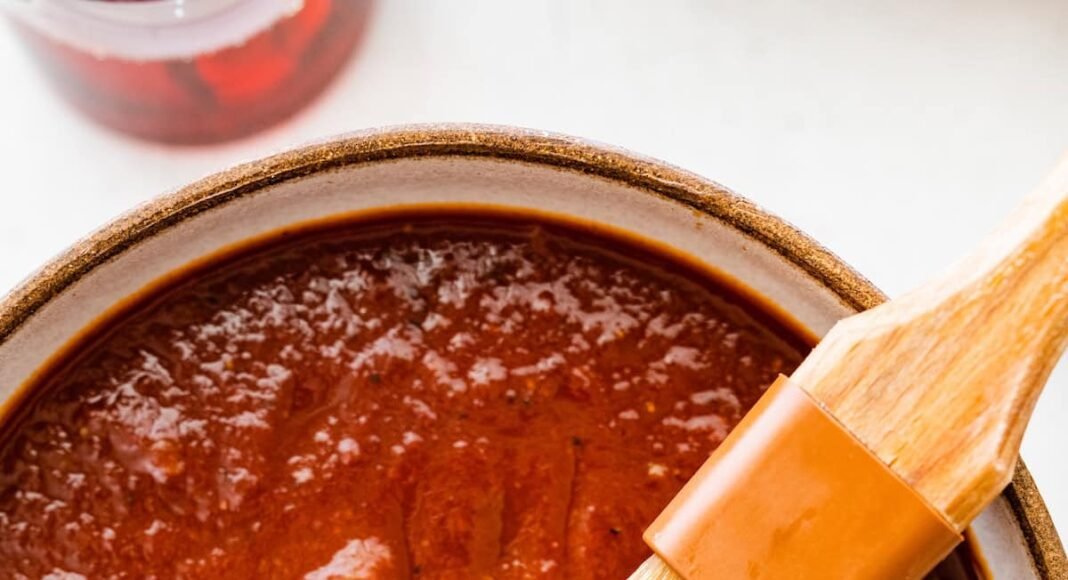 A bowl filled with homemade BBQ sauce with a small brush in the sauce.
